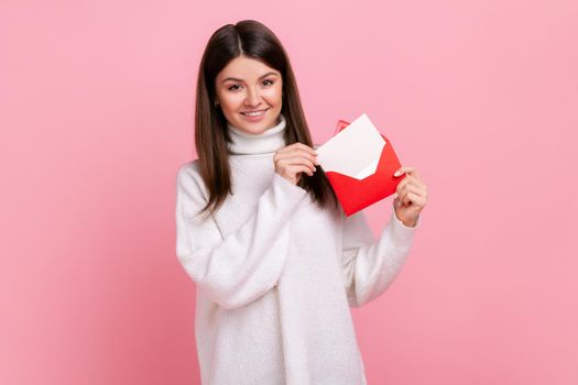 Portrait of woman standing, holding envelope and looking at camera with toothy smile and enjoying.