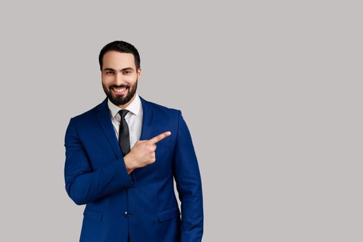 Bearded man pointing finger away with toothy smile on face, empty space for your advertisement.