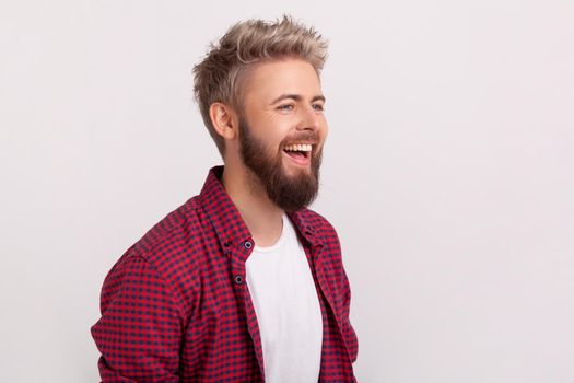 Portrait of joyful caucasian young man with beard and checkered shirt laughing, good mood and humor