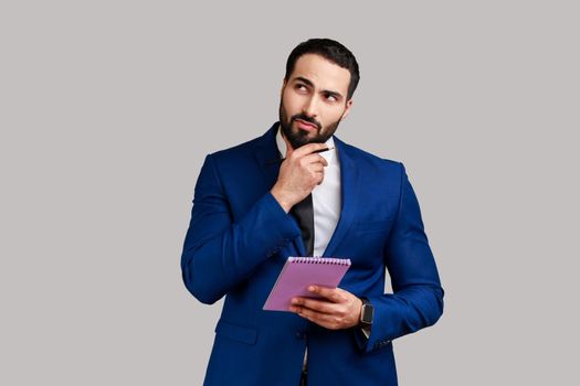 Man standing with thoughtful expression holding paper notebook, pondering business idea future plans