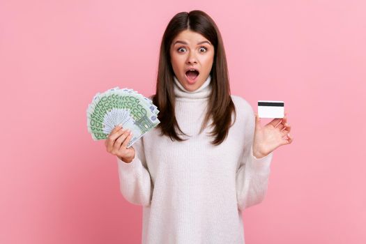 Surprised female holds credit card and big fan of euro banknotes, banking, earning big sum of money.
