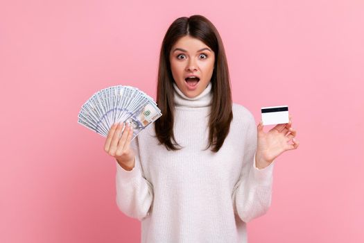 Shocked woman with dark hair holding fan of dollar banknotes and credit card, earning money, banking