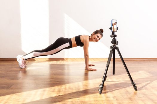 Coach teaching correct technique of doing plank exercise online, recording video on phone camera.