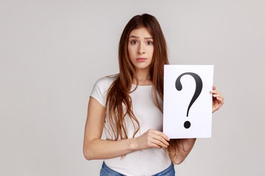Confused thoughtful woman looking at camera, holding paper with question mark, thinks about tasks.