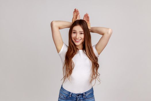 Amusing woman showing rabbit ears gesture on head and looking with childish carefree expression.