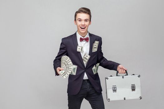 Portrait of ecstatic millionaire holding bunch of money and suitcase, lottery winner. white background