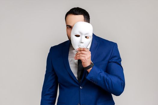 Man holding white mask, covering face standing with serious expression multiple personality disorder