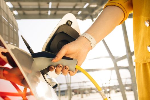 Woman hand inserts power cable supply to charge electric or EV car. Female plugging an electric car or EV at electric charging station