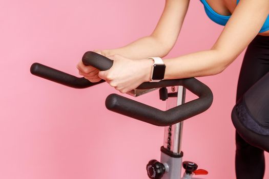 Closeup portrait of unknown woman hands with smartwatch on sport apparatus, riding exercise bike.