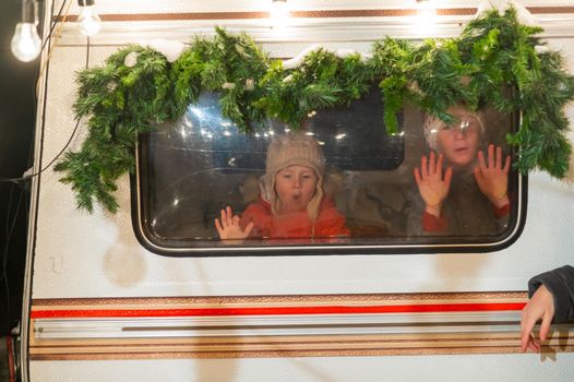 Two boys look out of the window of a Christmas-decorated camper.