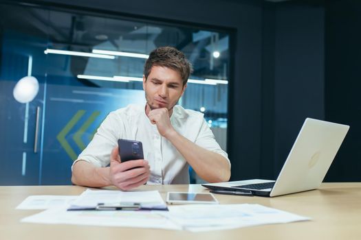 Upset and thinking man working in office, businessman looking at phone screen reading