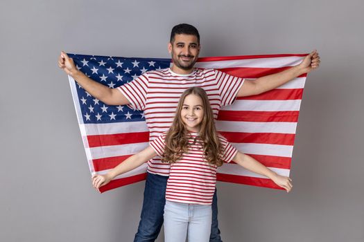Father and daughter in striped T-shirts holding big usa flag, relocation to United States of America