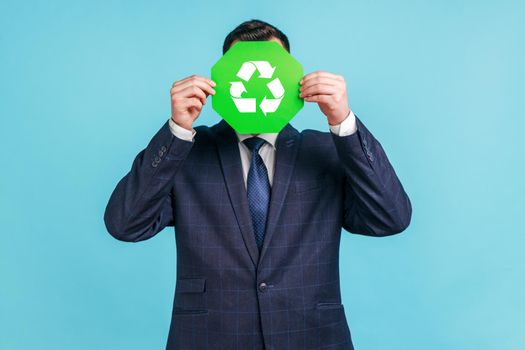 Unknown male person wearing official style suit hiding face behind green recycling sign, garbage sorting and environment protection, thinking green.