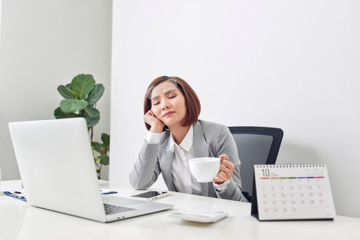 Tired young businesswoman taking a moment to relax at her desk with her eyes closed and head resting on her hand 