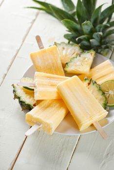 Yellow fruit popsicles on a plate. Top view over a white wood background.