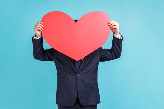 Portrait of anonymous wearing official style suit hiding behind large red paper heart, holding symbol of love affection fondness, love concept.
