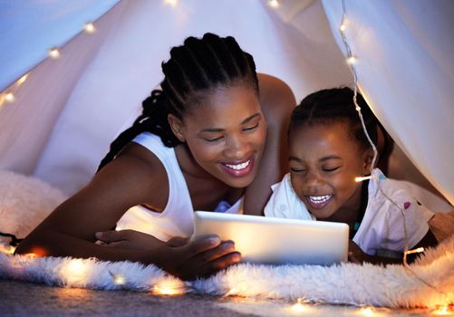 Its their tradition to read bedtime stories together. a mother and her daughter using a digital tablet together while relaxing under a blanket fort at home.