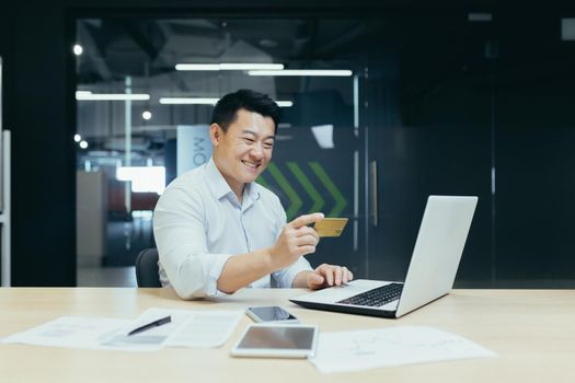 Happy Asian businessman working in modern office, man making online money transfer