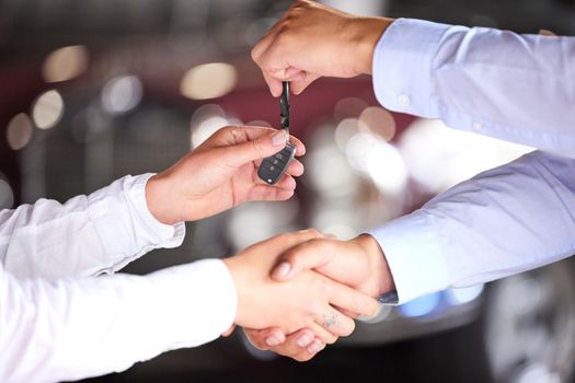 The handover. an unrecognizable car salesman shaking hands with a customer on the showroom floor of his car dealership.
