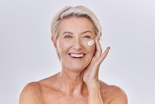 Portrait of one happy mature caucasian woman posing topless against a purple copyspace background. Ageing woman applying cream, moisturiser, sunblock during a skincare routine in a studio