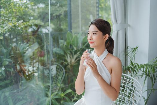 Asian lady drinking glass of milk while looking out the window with copy space