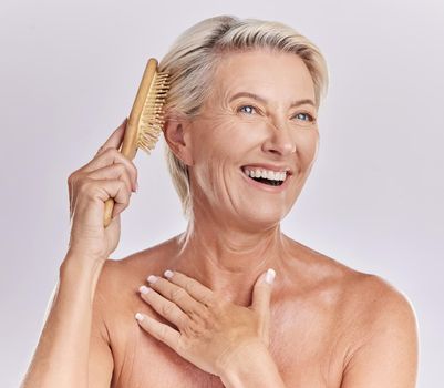 One mature caucasian woman brushing her hair to remove knots and tangles against a purple studio background. Happy older woman styling her hair
