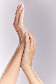 Closeup of unknown caucasian woman with soft skin showing manicured hands while isolated against a grey studio background. Two feminine hands raised and touching after beauty treatment