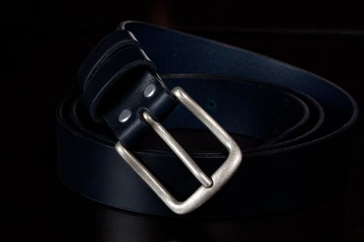 Leather belt with a metal buckle on a dark background close-up.
