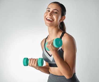 Stimulating muscle growth for a toned body. Studio portrait of a sporty young woman exercising with dumbbells against a grey a background.