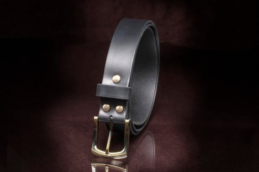 Leather belt with a metal buckle close-up on a dark background.
