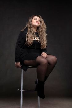 Beautiful fat woman with long curly hair in black clothes on a gray background. Plus size model girl.