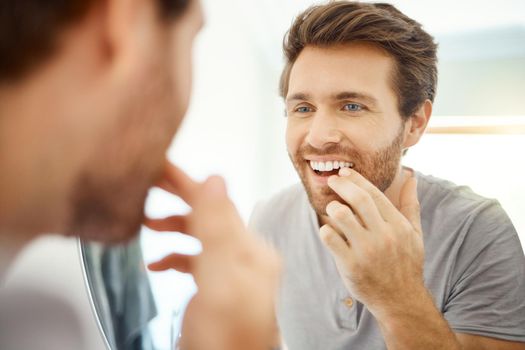 One handsome man checking his teeth in a bathroom at home. Caucasian male cleaning his teeth and looking in a mirror in his apartment.
