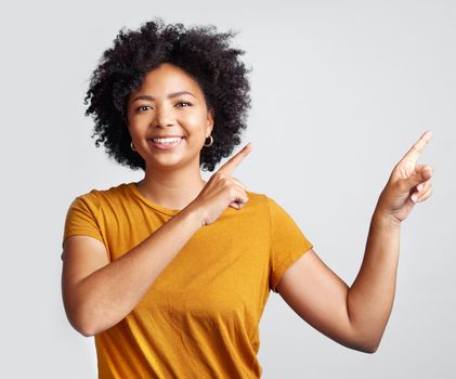 Use this to your advantage. a young woman pointing at copy-space against a grey background.