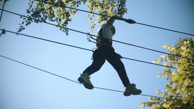 Rope adventure - slim woman walks on the suspension rope bridge