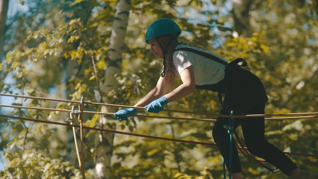 A woman in helmet crossing the rope bridge - an entertainment attraction in the forest