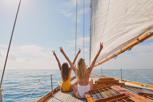 Two cheerful friends with arms raised making peace signs celebrating on boat cruise together. Two excited women in swimwear on holiday cruise celebrating cheering making peace signs in the air