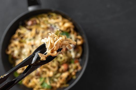 Italian fettuccini pasta close-up. Black pasta tongs with pasta. Pasta alfredo with mushrooms