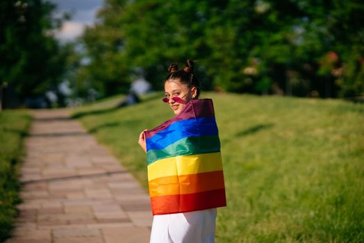 Young woman with lgbt pride flag walking in the park.