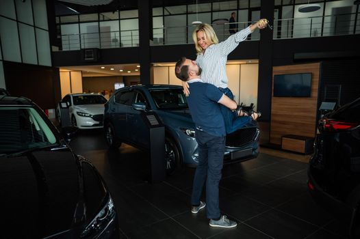 Happy caucasian couple hugging while buying a new car in a car dealership.