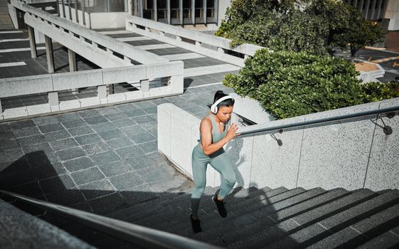 Young mixed race female athlete wearing headphones listening to music and running up stairs outside in the city. Exercise is good for your health and wellbeing