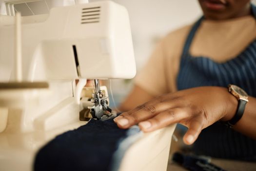 Closeup of hands of tailor using sewing machine. Fashion designer feeding denim through sewing machine. Hand of a seamstress stitching a piece of material. Creative businesswoman working in a studio