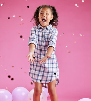 A pretty little mixed race girl with curly hair celebrating and winning against a pink copyspace background in a studio. African child looking excited at a gender reveal party with confetti