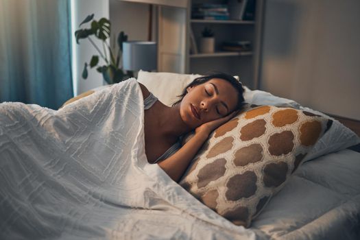 A beautiful young mixed race woman sleeping in a soft comfortable bed at home. One hispanic female feeling exhausted and resting in a comforting bed