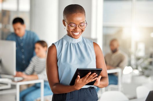 Cheerful african american businesswoman working on a digital tablet at work. Joyful black female businessperson using social media on a digital tablet. Businessperson checking an email on a digital tablet