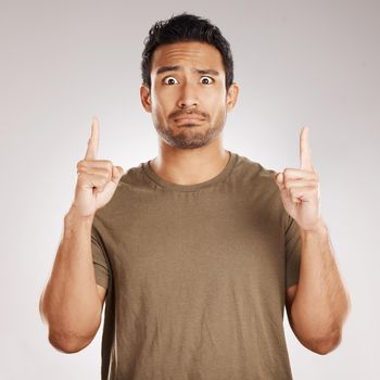 Handsome young mixed race man pointing towards copyspace while standing in studio isolated against a grey background. Unsure hispanic male advertising or endorsing your product, company or idea