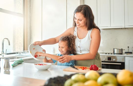 Cheerful mother and little daughter having fun cooking together in the kitchen. Mom and child cutting vegetables preparing a salad