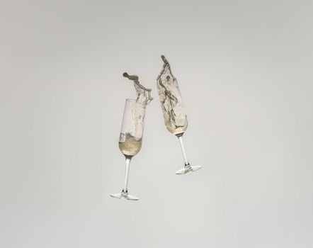 Splash of two crystal glasses toasting with champagne for a celebration. Splash on white cut-out background.