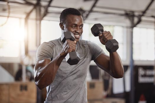 Smiling young african american athlete lifting dumbbells during arm workout in gym. Strong, fit, active happy black man training with weights in health and sport club. Weightlifting exercise routine