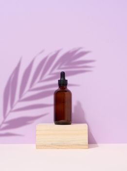 Brown glass bottle with a pipette on purple background. Palm leaf shadow