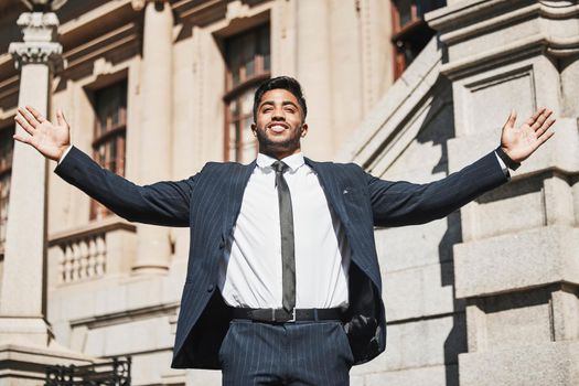 What freedom feels like. a handsome young businessman standing with his arms outstretched in the city.
